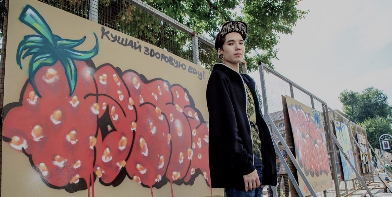 Художник граффити стоит около своих работ